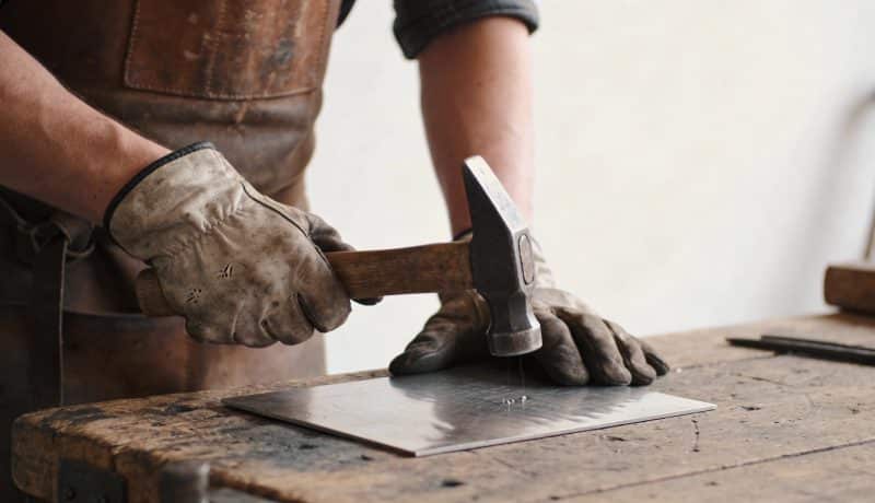 artisan martelant une fine plaque de metal