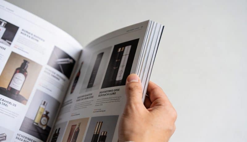 main tenant un magazine ouvert rempli de publicites