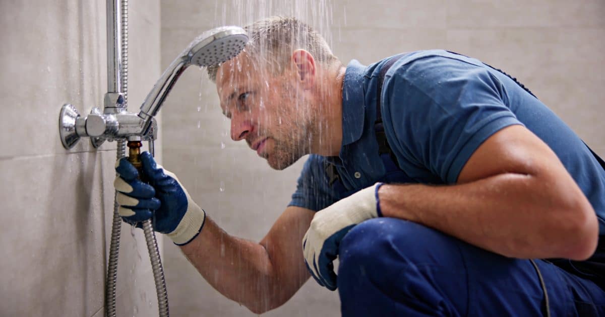 plombier agenouille sous douche examinant fuite eau