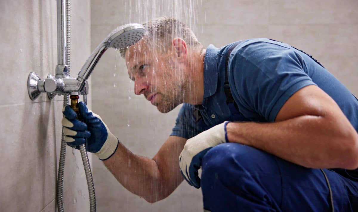 plombier agenouille sous douche examinant fuite eau