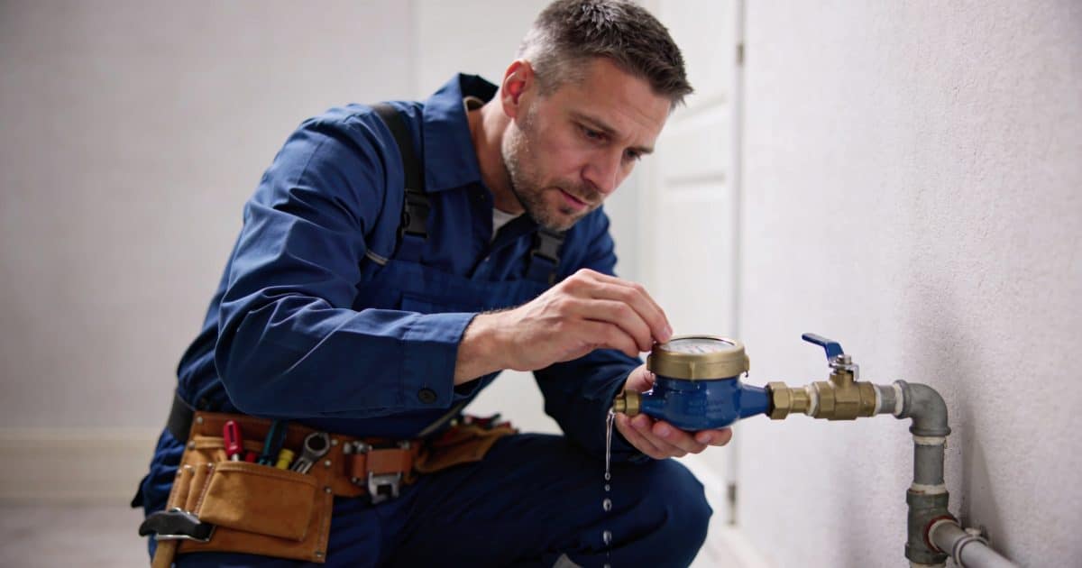 Plombier accroupi inspectant un compteur deau qui fuit