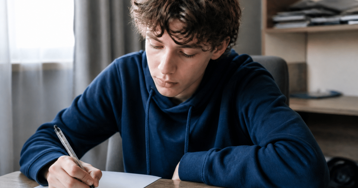 Adolescent assis a un bureau tenant un stylo