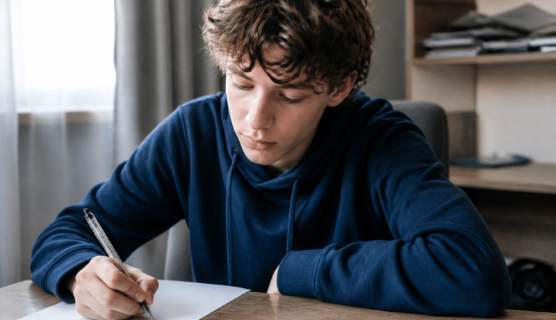 Adolescent assis a un bureau tenant un stylo