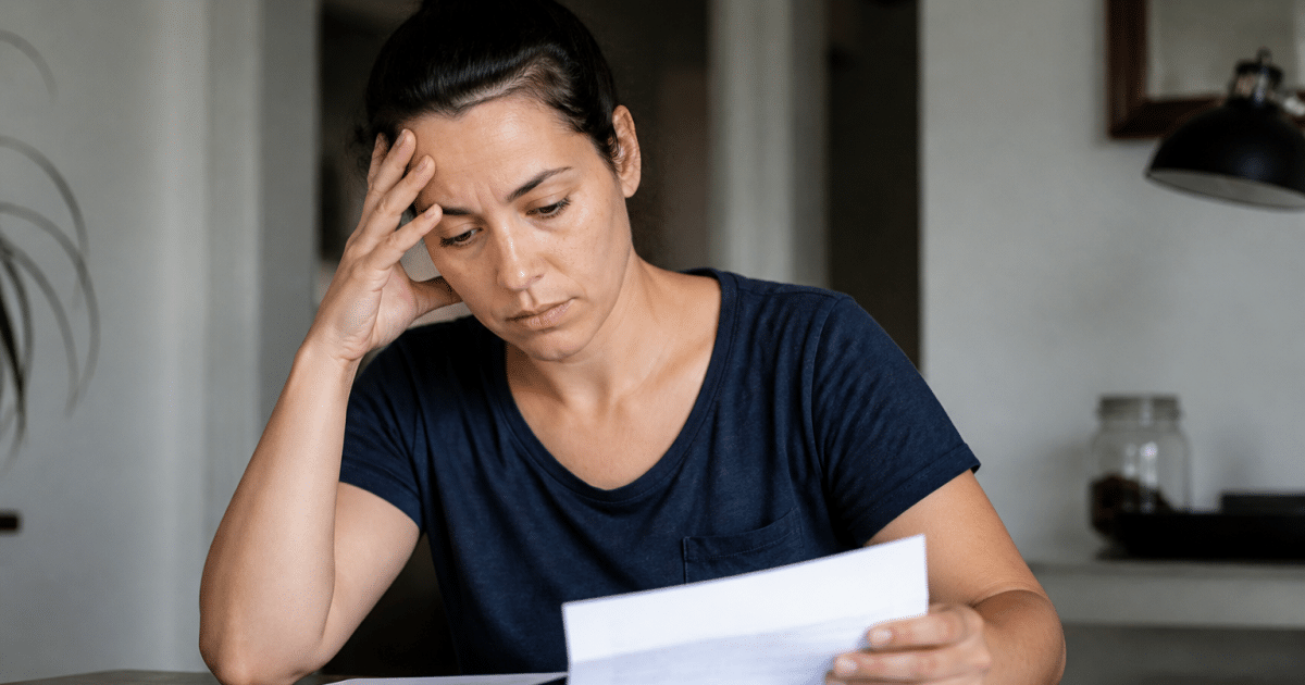 Femme seule tenant documents financiers sur table.