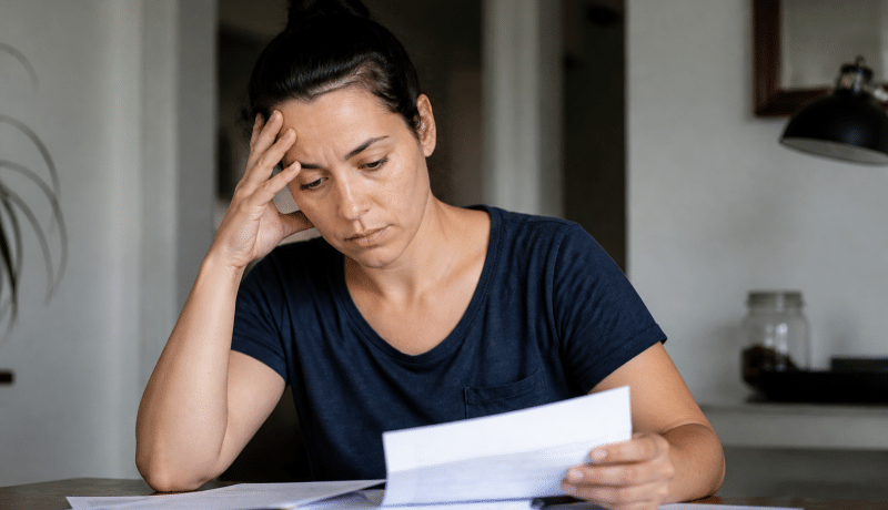Femme seule tenant documents financiers sur table.