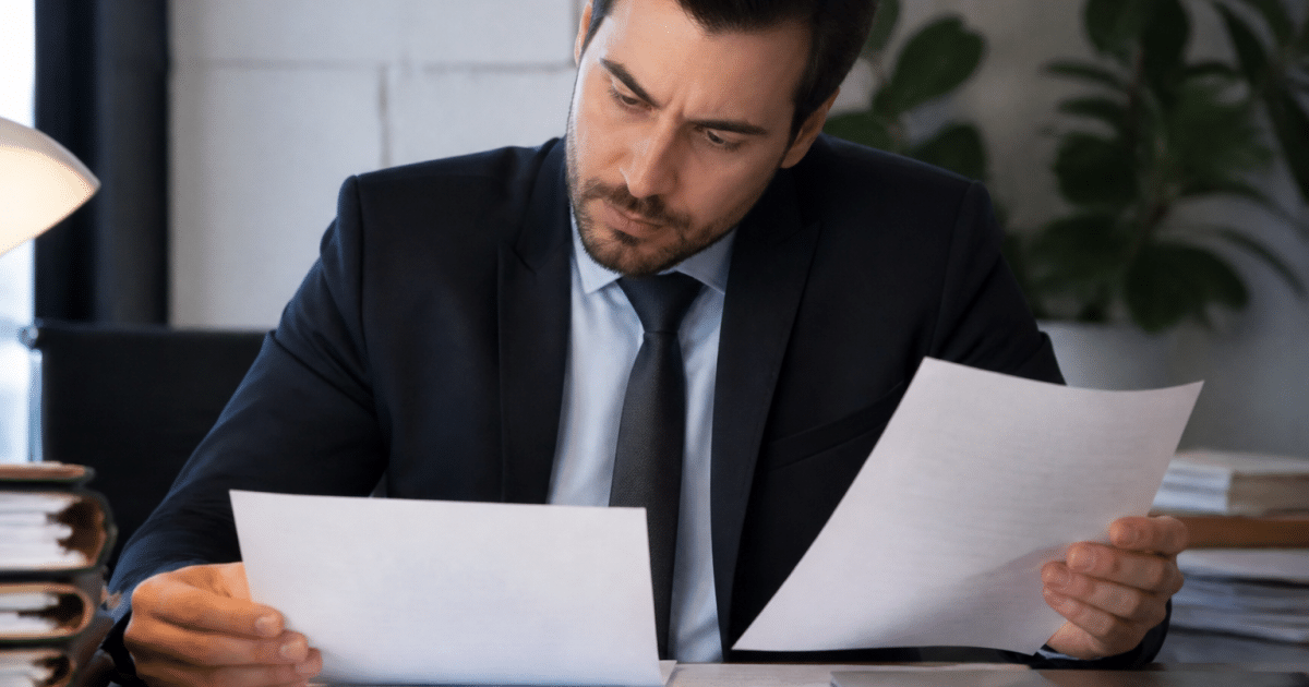 Huissier en costume examinant des documents financiers sur bureau.