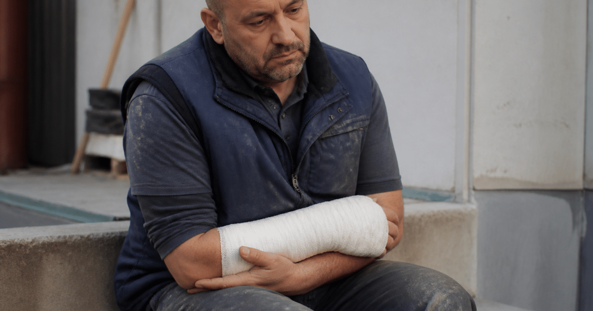 Ouvrier assis tenant son bras bandé après blessure.