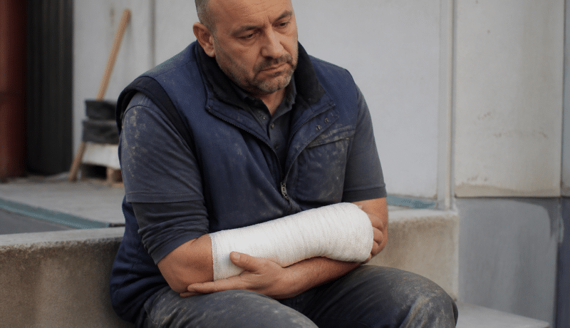 Ouvrier assis tenant son bras bandé après blessure.