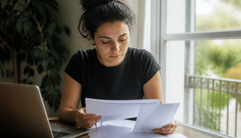 Personne assise consultant documents financiers avec relevé bancaire.