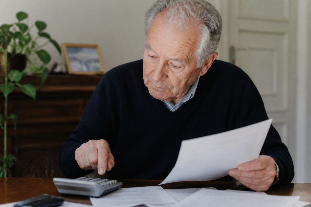 Personne âgée examinant documents fiscaux avec calculatrice grise