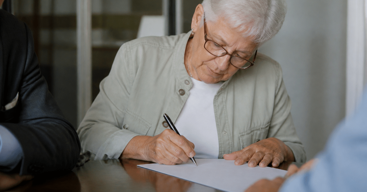 Personne âgée signant des documents notariés importants.
