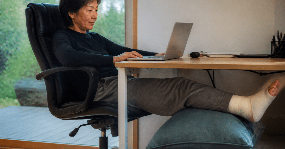 Personne assise au bureau avec jambe elevee sur coussin.