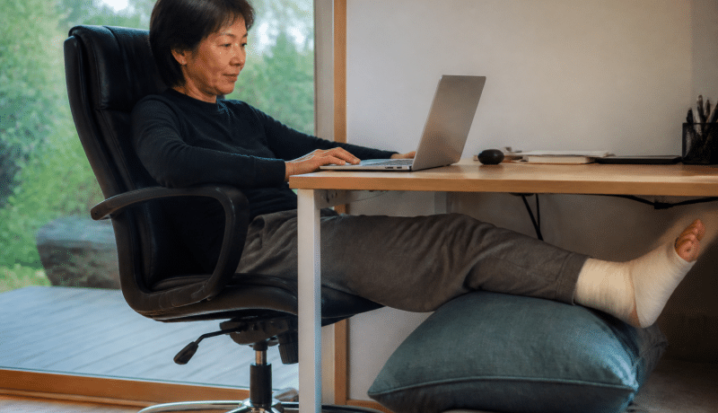 Personne assise au bureau avec jambe elevee sur coussin.