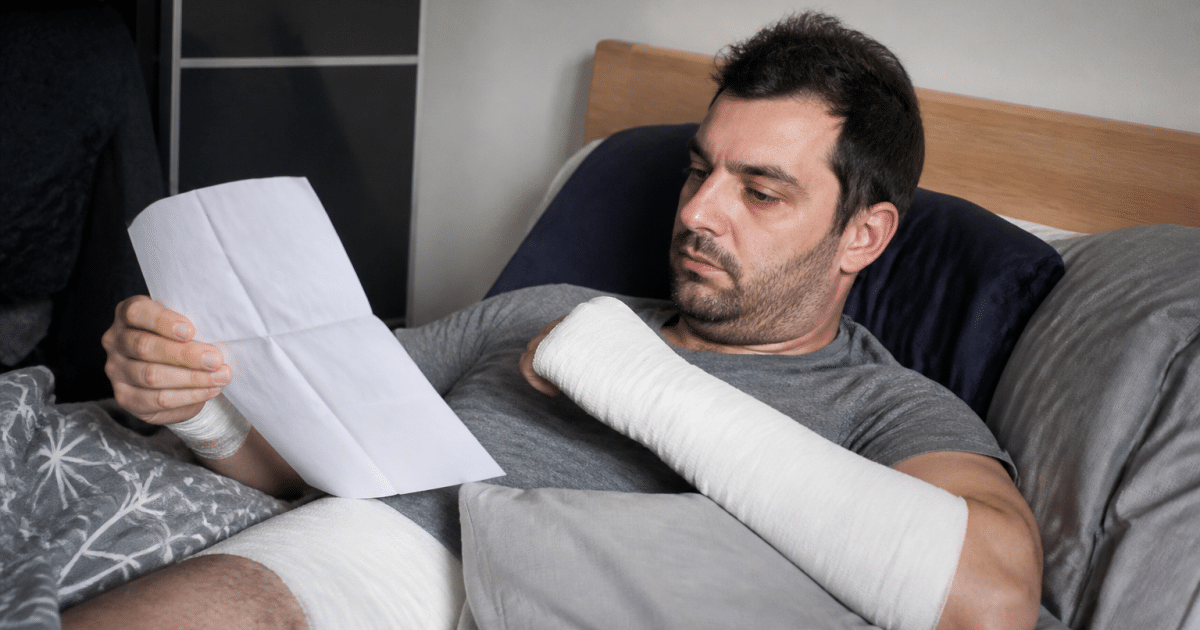 Travailleur immobilise au lit avec pansements et documents administratifs.